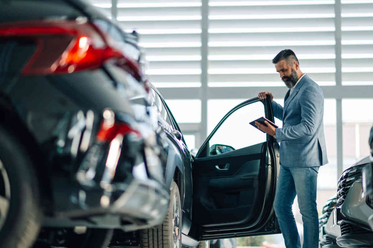 Un homme se tient à côté d’une nouvelle voiture et regarde son smartphone.